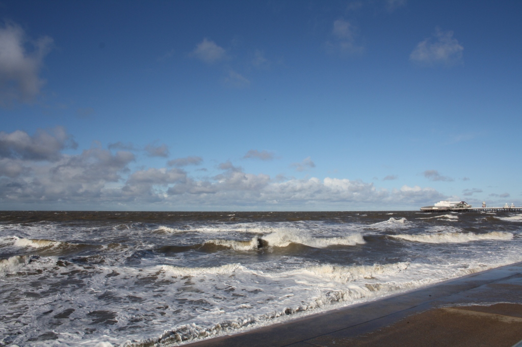 Blue sky with fluffy clouds towards the horizon above a stormy sea rolling onto the beach